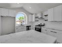 Bright kitchen featuring white cabinets, marble countertops, stainless appliances, and a large arched window at 1638 Candice St, Las Vegas, NV 89156
