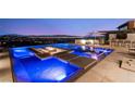 Modern blue pool with built-in lounging area and fire pit, overlooks the city lights at night at 507 Serenity Point Dr, Henderson, NV 89012