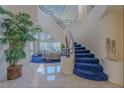 Bright foyer with grand staircase, blue carpeted steps, light tile flooring, and view to living room at 8196 Horseshoe Bend Ln, Las Vegas, NV 89113