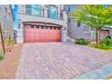 Paver driveway leading to a home with a striking red garage door, landscaped yard, and a welcoming facade at 7032 Steele Canyon St, Las Vegas, NV 89118