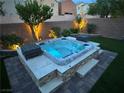 Modern hot tub with tiered platform, illuminated at night, amidst landscaping and exterior stone wall at 7424 Rainford St, Las Vegas, NV 89148