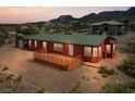 A single-story red home with a green roof and wooden deck, surrounded by desert landscaping at 70 Camp Bonanza Rd, Las Vegas, NV 89124
