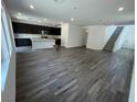 Open-concept living room with gray wood-look tile flooring, kitchen island, and staircase at 64 Via Montoro, Henderson, NV 89011