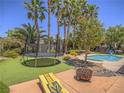 Private backyard features mature palm trees, a pool, a trampoline and a grassy area for relaxing at 8106 Eagle Clan Ct, Las Vegas, NV 89131
