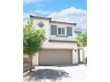 Inviting two-story home featuring a tan exterior, a two-car garage and a lovely tree in the front yard at 1703 Game Garden Rd, North Las Vegas, NV 89031