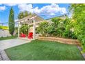 Manicured backyard with a pergola, artificial grass, garden beds, and red Adirondack chairs at 5553 Coral Gate St, Las Vegas, NV 89148