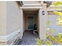 Inviting front porch area with a teal door and seating, complemented by paver flooring and stone facade accents at 7616 Quail Dust St, North Las Vegas, NV 89084