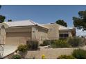 A single-story beige home featuring a two-car garage, desert landscape, and gated yard at 471 Fallwood Ln, Las Vegas, NV 89107
