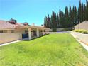 A spacious backyard with lush lawn and tall privacy trees, featuring a covered patio at 1536 Brocado Ln, Las Vegas, NV 89117