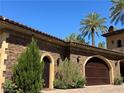 Charming stone and stucco home featuring an arched garage door and manicured greenery at 1800 Amarone Way, Henderson, NV 89012