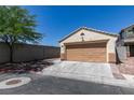 A single-car garage with a neutral tan door and trim matches the home's exterior, complemented by a lengthy driveway and mature tree at 1905 Eskam St, Las Vegas, NV 89156
