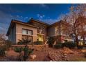 Charming two-story house featuring stone detailing, manicured greenery, and enhanced outdoor lighting at dusk at 3042 Hammerwood Dr, Las Vegas, NV 89135
