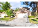 Home exterior with a two-car garage, mature trees, green grass, and a concrete driveway at 912 Pro Players Dr, Las Vegas, NV 89134
