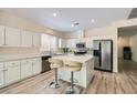 Bright kitchen featuring white cabinets, stainless steel appliances, a center island with seating, and wood-look floors at 11074 Caramel Crest Ct, Las Vegas, NV 89135