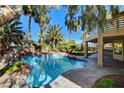 Backyard oasis featuring a sparkling pool with rock features, palm trees, and a covered patio area at 902 Cripple Creek Ct, Henderson, NV 89014