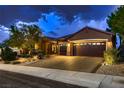 Well-lit home exterior featuring a three-car garage, desert landscaping, and tiled roof at 2786 Scotts Valley Dr, Henderson, NV 89052