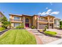 Two-story tan home with a green lawn, brick driveway, and red front door at 3738 Amber Lantern Cir, Las Vegas, NV 89147