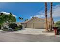 Charming single-story house featuring a well-manicured lawn, desert landscaping, and palm trees against a bright blue sky at 819 Sandsprings St, Henderson, NV 89011