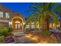 A well-lit front entrance with a stone path, lush landscaping, and arched doorway with glass paneled doors at 4045 Abernethy Forest Pl, Las Vegas, NV 89141
