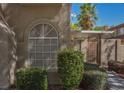 A charming architectural detail featuring an arched window, stucco wall, and lush green landscaping at 7716 Bauble Ave, Las Vegas, NV 89128