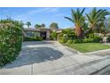 Beautiful single story home featuring lush landscaping, mature palm trees, and a concrete driveway at 10320 Luxembourg Ave, Las Vegas, NV 89145