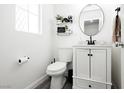 Stylish half bath featuring white vanity with black hardware, modern round mirror, and wood-look tile flooring at 551 Swiss Cottage Ave, Las Vegas, NV 89178