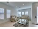 Bright living room features light colored sofas, a glass coffee table, herringbone floors, and large windows at 9844 Kings Glen St, Las Vegas, NV 89141