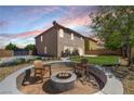 Outdoor fire pit area with wooden chairs and lush grass at a charming home with views of a colorful dusk sky at 10343 Beallsville St, Las Vegas, NV 89141