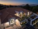 Luxury home boasts a tile roof, manicured landscape, and outdoor seating with a fire pit at dusk at 1429 Iron Hills Ln, Las Vegas, NV 89134
