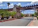 Community entrance with stone accents, lush landscaping, and palm trees under a bright, cloudy sky at 4990 River Glen Dr # 171, Las Vegas, NV 89103