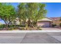 Charming single-story home featuring mature trees and desert landscaping in the front yard under a bright blue sky at 1897 Holdenville St, Henderson, NV 89052