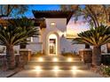 Inviting front entrance with arched doorway, illuminated steps, and mature palm trees under a colorful dusk sky at 11906 Port Labelle Dr, Las Vegas, NV 89141