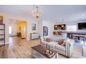 Bright living room featuring hardwood floors, elegant chandelier, and a seamless transition into a modern kitchen with bar seating at 10434 Rose Palisade St, Las Vegas, NV 89141