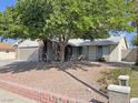 Single-story home featuring a two-car garage, mature trees, and rock landscaping at 1441 Bronco Rd, Boulder City, NV 89005