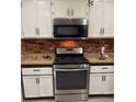 Well-lit kitchen featuring stainless steel range, microwave, white cabinetry, and tasteful brick backsplash at 3128 Spring City Ave, North Las Vegas, NV 89081