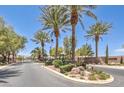 Landscaped median with palm trees and greenery leads to a gated community entrance under a clear blue sky at 6821 Sleepy Pine St, Las Vegas, NV 89130
