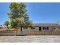 Home exterior featuring large tree, neutral paint, black trim and a concrete block fence in front at 2315 Lincoln Rd, Las Vegas, NV 89115