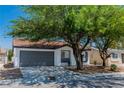 Charming single-story home with mature trees, a gray garage door and desert landscaping at 2112 Hollow Oak Ave, North Las Vegas, NV 89031