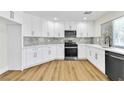 Renovated kitchen with white cabinets, stainless steel appliances, gray backsplash and light vinyl flooring at 2112 Hollow Oak Ave, North Las Vegas, NV 89031