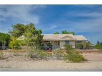 Charming single-story home with a tiled roof, complemented by a lush green landscape and a clear blue sky at 6990 W Richmar Ave, Las Vegas, NV 89178