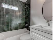 Modern bathroom featuring green tiled shower over tub and white vanity with round mirror at 1504 E Ogden Ave, Las Vegas, NV 89101