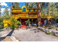 Yellow two-story house with wrap-around deck, red stairs, and mature trees at 362 Rainbow Canyon Blvd, Las Vegas, NV 89124