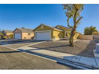 Tan one-story house with a white garage door and landscaping at 2210 Cool River Ct, North Las Vegas, NV 89032