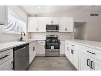 Modern kitchen featuring white cabinets, stainless steel appliances, and stylish gray wood-look flooring at 421 Box Elder Way, Henderson, NV 89015