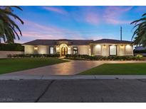 Stunning single story home with well-manicured landscaping, a circular driveway, and elegant lighting at twilight at 5555 W Desert Inn Rd, Las Vegas, NV 89146