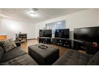 Open living room with wood floors, gray sofa, large window, and three large televisions at 271 Greenbriar Townhouse Way, Las Vegas, NV 89121