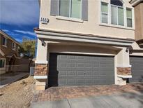 Two-car garage featuring gray door, stone accents, and brick paver driveway at 6448 Elwood Mead Ave # 103, Las Vegas, NV 89156