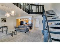 Open-concept living room with carpet, gray sofa, chandelier lighting, and view of the kitchen and staircase at 4047 Village Sq, Las Vegas, NV 89121