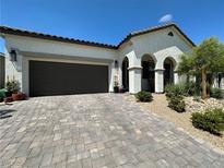 Inviting home featuring a two-car garage, paver driveway, arched entrance, and desert landscaping at 10064 Ocher Valley Ave, Las Vegas, NV 89178