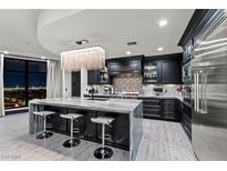 Modern kitchen boasts an island with seating, dark cabinetry, and a stunning chandelier overlooking city views at 9101 Alta Dr # 1206, Las Vegas, NV 89145